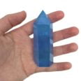 A person holding a blue quartz point, also known as an Aura Quartz Tower, in their hand.