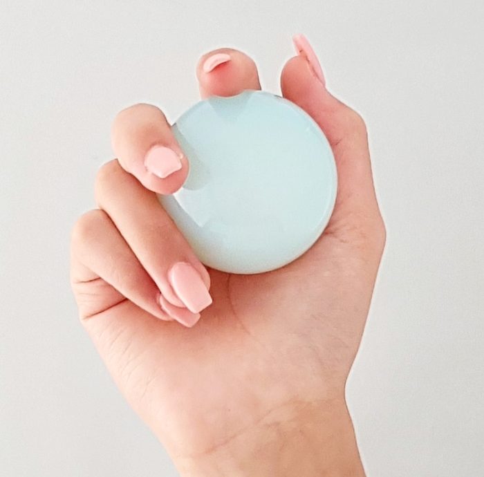 A hand delicately cradling a shimmering Opalite Solid Ball in a soothing shade of blue.