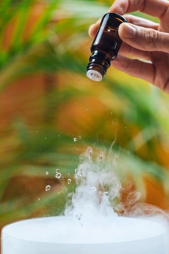 An Aroma Ultrasonic Electric Diffuser is pouring a bottle of essential oil into a bowl of water, creating an aromatic mist in the air.