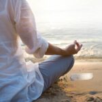 A woman meditating on the beach while finding serenity and peace with the Selenite Meditation Bar.